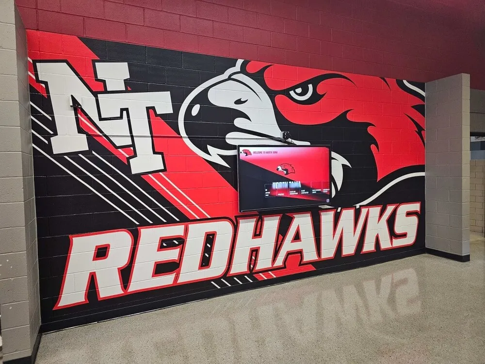 School hallway featuring Redhawks athletic mural with integrated digital display screen School athletic mural and display